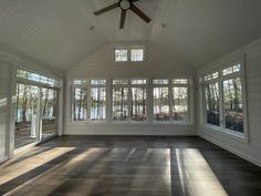 an empty room with windows and a ceiling fan in the center, along with wood flooring