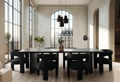 a dining room table surrounded by black chairs and large windows with arched glass panes