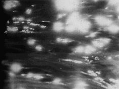 blurry black and white photograph of street lights in the rain at night time, taken from an airplane window