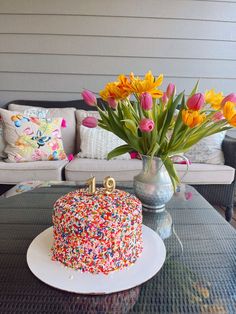 a birthday cake with sprinkles and flowers in a vase on a table