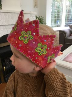 a young boy wearing a red crown with green flowers on it