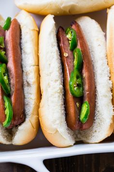 three hot dogs in buns with green peppers and jalapenos on them