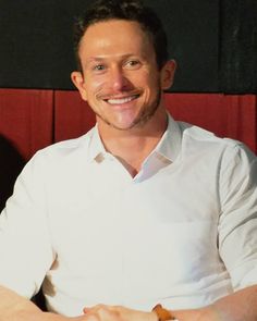 a man sitting at a table with food in his hand and smiling for the camera