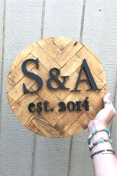 a person holding up a wooden sign that says s & a, and has the initials on it