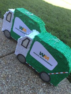 two green trucks made out of construction paper on the ground next to grass and sidewalk