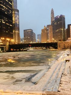 the city skyline is lit up at night with ice on the water and snow covered ground