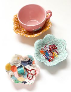 two small dishes with scissors on them next to a cup and saucer filled with candy