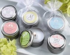 six personalized candles in tins on a table with flowers and ribbon around them