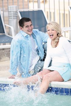 a man and woman sitting on the edge of a swimming pool with splashing water