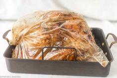 a turkey wrapped in plastic sitting on top of a pan