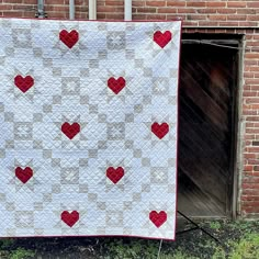 a white quilt with red hearts on it in front of a brick wall and door