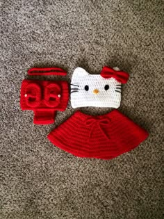 a crocheted hello kitty hat and mitten set on the floor with grey carpet