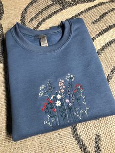 a blue t - shirt with flowers embroidered on the front and back, sitting on a couch