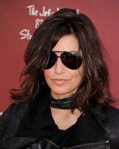 a woman with sunglasses and a leather jacket on posing for the camera in front of a red background