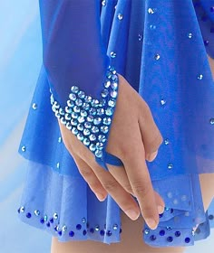 a close up of a person's hand wearing a blue dress with beads on it