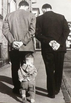 two men walking down the street with a small child in front of them and another man holding his hand