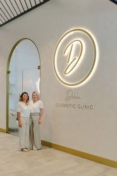 two women standing next to each other in front of a white and gold sign that says dolce cosmetic clinic