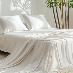 an unmade bed with white sheets and pillows on top of it next to a potted plant