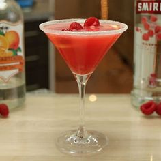 a red drink in a martini glass with a raspberry garnish on the rim