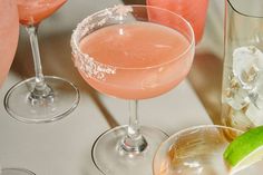 two cocktail glasses with different types of drinks next to each other on a white surface