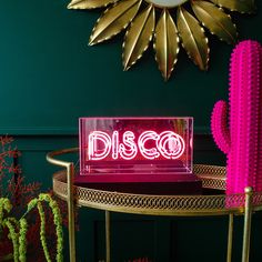 a neon sign sitting on top of a table next to a cactus