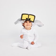 a baby sitting on the floor wearing a white bodysuit with sunglasses on it's head