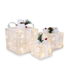 three white lighted presents with bows and pine cones on the top, sitting next to each other