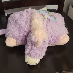 a purple stuffed animal laying on top of a wooden table next to a black chair