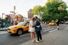 a man and woman standing on the side of a road next to a yellow taxi