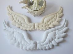 three angel wings and a mirror on a white table top with the reflection of an angel in it