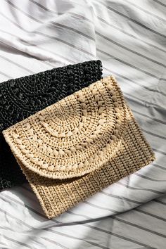 two straw bags sitting on top of a bed next to each other, one black and one beige