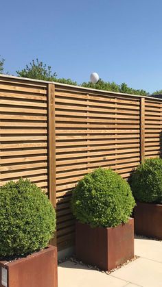 three large planters are next to a wooden fence with balls on the top one