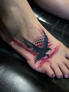 a bird tattoo on the foot of a person with red and black ink splatters