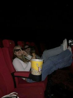 two women sitting in red chairs with popcorn buckets