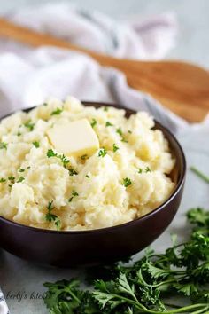 mashed potatoes with butter and parsley in a brown bowl on a white surface