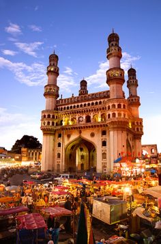 an outdoor market with lots of people and tents in front of it at dusk time