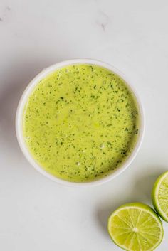 a bowl of broccoli soup next to two limes on a white surface