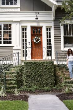 a woman standing in front of a house with a wreath on it's door