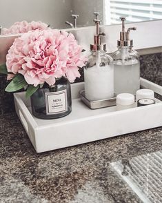 a pink flower sitting on top of a bathroom counter next to two soap dispensers