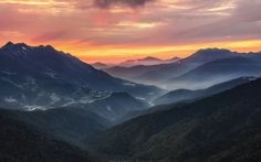 the sun is setting in the mountains with clouds and trees on it's sides