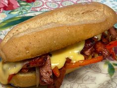 a sandwich with meat, cheese and peppers on a floral tableclothed plate next to a cup