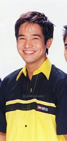 two young men standing next to each other in front of a white wall and smiling at the camera