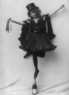 an old photo of a woman in a dress and top hat holding a wine bottle