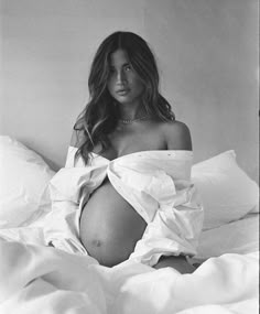 a pregnant woman sitting on top of a bed in a white dress with her stomach exposed