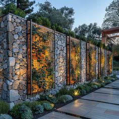 a stone wall with plants growing on it and lights shining in the windows behind it