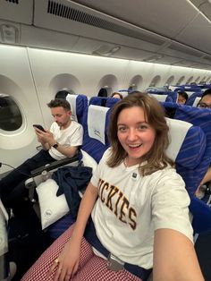 a woman sitting on an airplane with two men in the back and one man looking at her phone