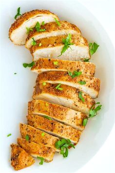 slices of chicken on a white plate with green garnishes and parsley