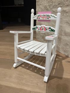 a white rocking chair sitting on top of a hard wood floor next to a wall