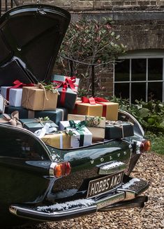 an old car is loaded with presents and wrapped in ribbon, sitting on the gravel