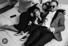 a man and woman laying on top of a bed next to a little boy wearing sunglasses